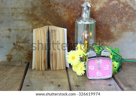 Vintage alarm clock, yellow flower, old book and lamplight on wooden table. Still Life
