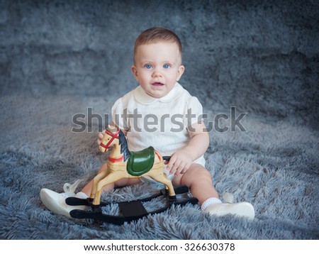 Cute boy on a gray background with a toy horse in his hands