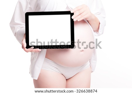 Pregnant woman close up with bared belly standing on a white background and holds a plate, picture with depth of field, selective focus on tablet