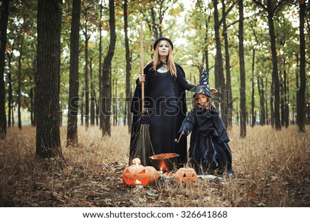 adult witch and small witch making magic in the wood. mother and daughter in halloween costumes