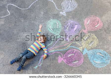 Cute little kid boy playing and flying with colorful balloons picture drawing with chalk. Creative leisure for children outdoors in summer, celebrating birthday