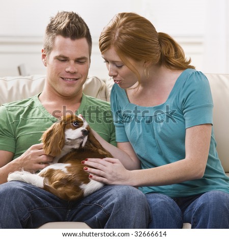 A young and attractive couple holding and petting a dog. Square framed photo.