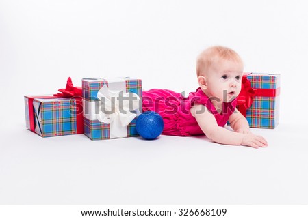 Cute girl lying on her stomach on a white background in a New Year's cap among Christmas balls, blue and red boxes with gifts, picture with depth of field