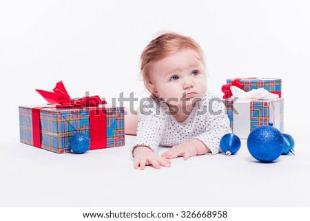 cute toddler is sitting in a New Year's red cap on white background unpacks a gift with a smile on his face, picture with depth of field