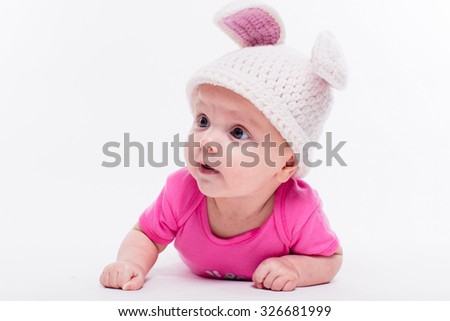 cute baby girl lying in a bright red T-shirt on a white background wearing a hat in the form of a Christmas bunny with pink ears and tail, with depth of field Photo