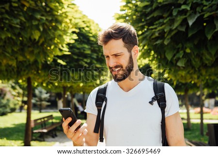 handsome student having  backpack and talking at mobile phone standing outside
