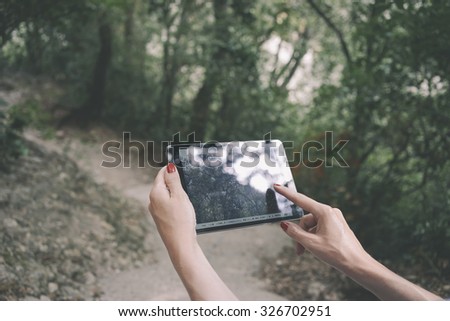 Cropped image with female's hands touching screen of digital tablet in a forest