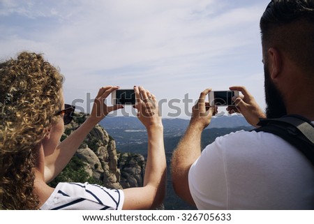 Young couple hiking in the mountains taking a picture of landscape on smart-phones