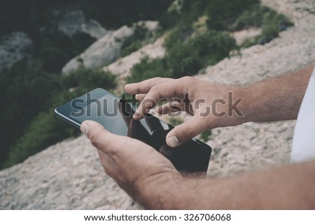 Cropped image with female's hands touching screen of digital tablet on the background of mountains