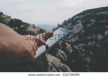 Cropped image with man's hands touching screen of digital tablet on the background of mountains