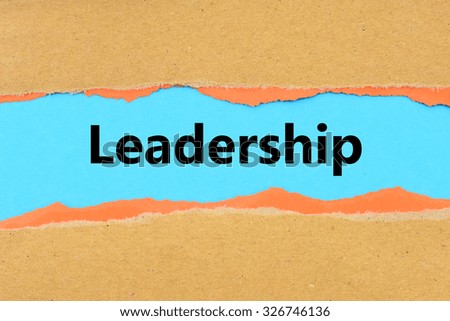 Torn brown and orange paper on blue surface with Leadership words.