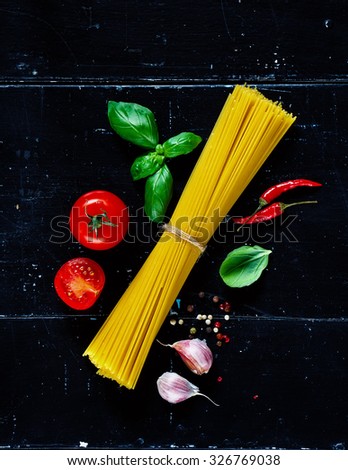 Pasta spaghetti, basil leaves and tomatoes with herbs on dark vintage background. Vegetarian food, diet, health or cooking concept.