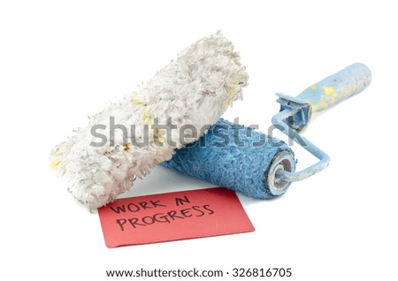 creative image of dirty and reused white and blue roller paint brush with white feather placed in front. work in progress on red paper isolated on white background