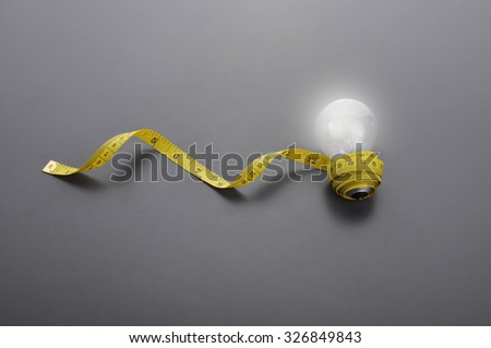 Lowlight key of light bulb and Yellow measuring tape on grey background