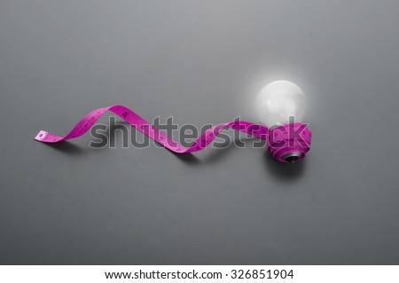 Lowlight key of light bulb and pink measuring tape on grey background