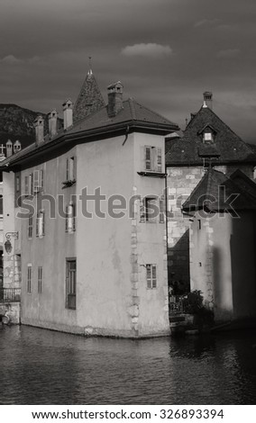 Houses over the canal in picturesque old town of Annecy (France) at  sunset in cloudy day. Majestic game of contrasting light and shadow. Aged photo. Black and white.