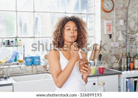 Mixed race girl indulging cheeky face eating chocolate spread from  jar using spoon savoring every  mouthful Royalty-Free Stock Photo #326899193