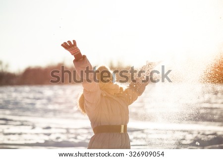 Girl throws snow up. Photographed in backlit. Silhouette. Girl in the park, around the snow. One can see a grain of snow fluttering around.