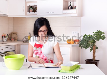 Young woman working in the kitchen, reading recipe for baking Royalty-Free Stock Photo #326927447