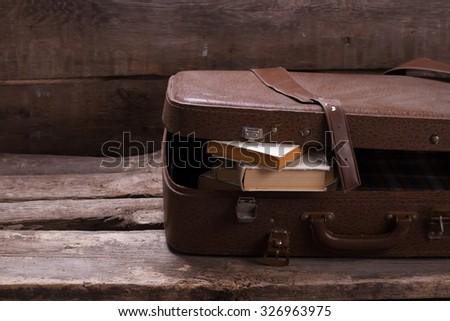 Old leather suitcase with books on vintage wooden background.