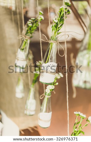 Closeup toned photo of decorated bottles with flowers hanging on twine