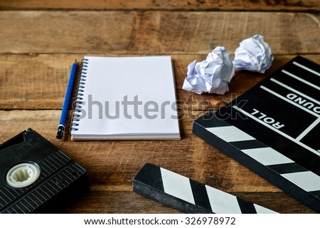 Movie clapper with notepad and pencil on wooden table