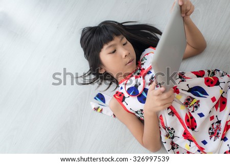 Child with tablet lying on floor. Girl playing laptop computer