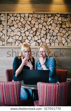 Two beautiful blond girls working on the laptop in coffee bar. 