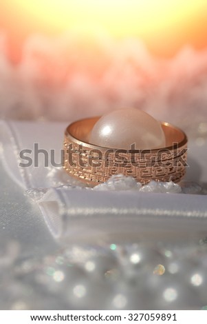 Closeup of one beautiful luxury golden engagement ring lying on soft white fabric with lace and pearl bead on wedding celebration indoor, vertical picture