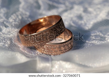 Closeup of two beautiful luxury golden engagement rings lying together on soft white fabric with lace on wedding celebration indoor, horizontal picture