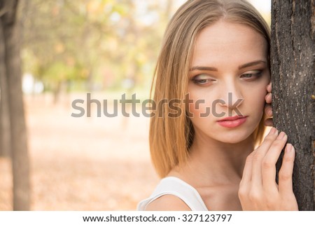 Sad dreamy Young adult woman stand in autumn park resting by two hands lie on a tree Close up portrait Empty copy space for inscription or other objects 