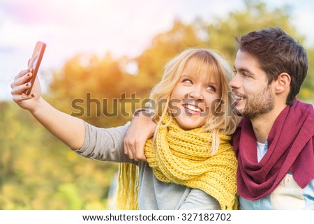 Fall in love couple friends taking selfie outdoor with warm sunshine colors - Beauty and freedom inspiration outdoors autumn vacations - Young people in four season clothes having fun with the phone