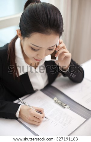 Businesswoman talking on the phone while signing documents