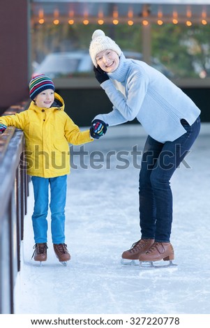 young mother teaching her little son ice skating at outdoor skating rink