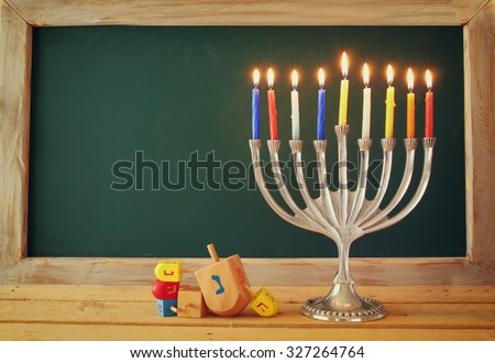low key image of jewish holiday Hanukkah with menorah (traditional Candelabra) and wooden dreidels spinning top with chalkboard background, room for text
