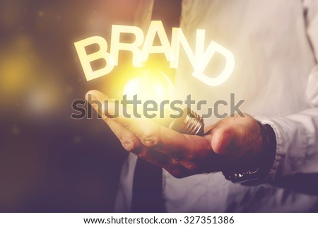 Brand idea concept with businessman holding light bulb, retro toned image, selective focus. Royalty-Free Stock Photo #327351386
