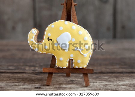 Homemade gingerbread cookie in the shape of yellow elephant with polka dots on a wooden background. Space for text and selective focus.
