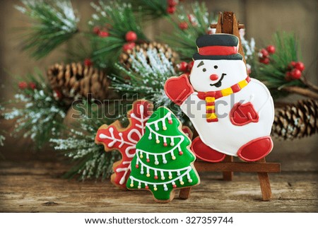 Homemade christmas gingerbreads painted as snowman, a red snowflake and Christmas tree with festive decoration on the wooden background with fir branches. Selective focus and place for text. Toned.