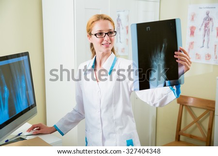 Smiling female doctor in glasses looking at x-ray at office and working at the computer
