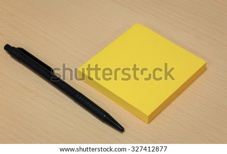 black pen,yellow paper on wood table background.