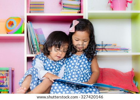 Child read, two cute little girls reading book together on bookshelf background