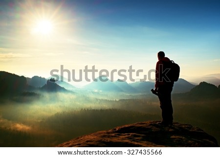 Tall adult  photographer think about picture at sunset in the misty mountains