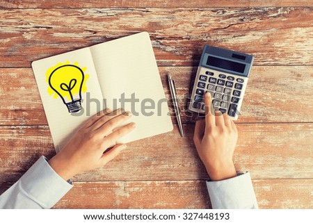 business idea, education, people and technology concept - close up of female hands with calculator, pen and lighting bulb drawing in notebook on table