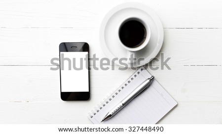 cellphone with notebook and coffee cup over white table