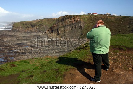 photographer on the top of the cliff taking a picture along the seashore