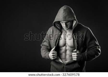 An athlete in a sports jacket with a hood on a dark background. A man shows his muscles revealing jacket. Photos for sporting magazines, posters and websites.
