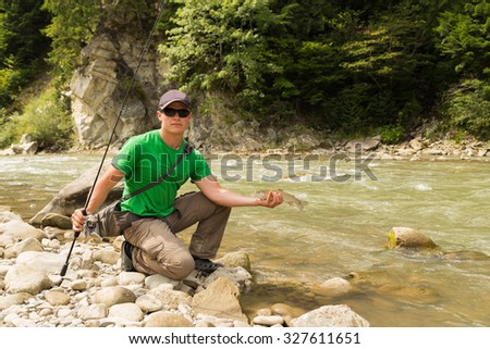 Man holds on a mountain river caught trout. Fishing on the mountain river. The beautiful landscape and beautiful fish. Photo for Natural magazines and websites.
