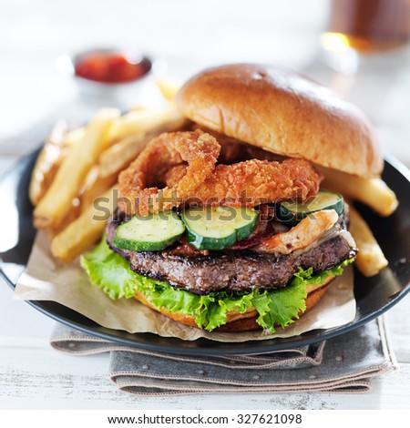 bacon barbecue burger topped with onion rings on white table served with fries