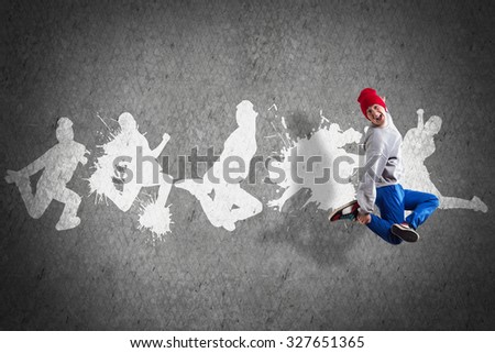 Young hip hop dancer in jump and silhouettes on gray wall