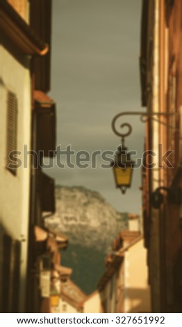 Blurred toned photo. View through the narrow medieval street on the mountains at background during sunset (Annecy, France). A game of  contrasting light and shadow. 